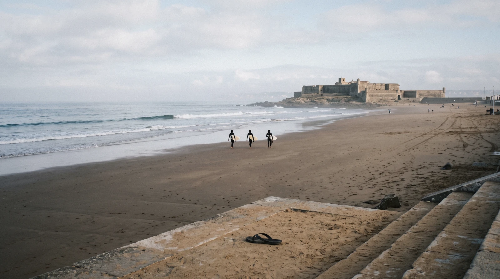 Praia de Carcavelos at nine on a September morning with the fort at the eastern end and the first surfers in the water, the nearest of the Lisbon beaches by train