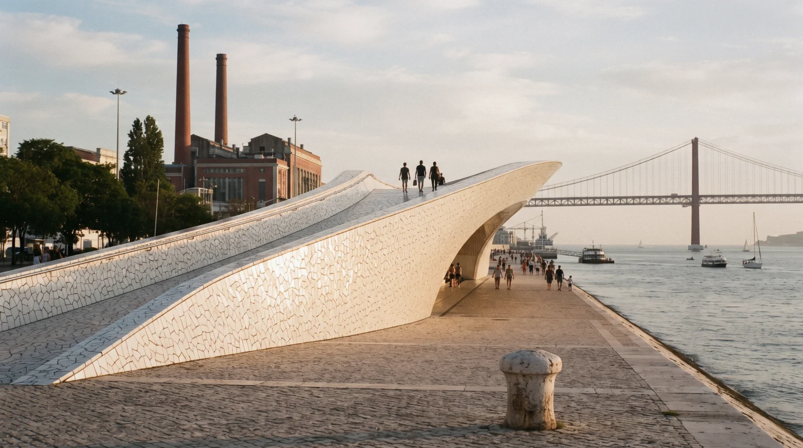 The white tiled wave of the MAAT museum on the Belém riverfront at 18:30 with the brick chimneys of the Tejo power station behind it, MAAT Museum Lisbon