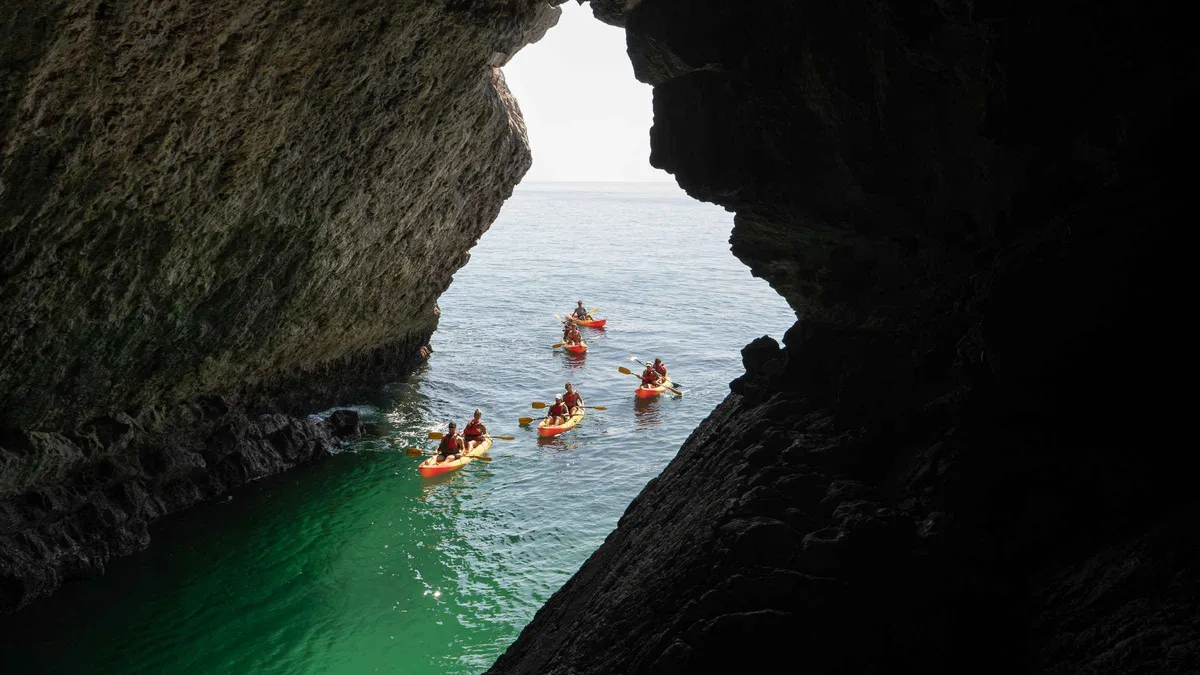 Kayakers paddling past limestone cliffs toward Ribeiro do Cavalo beach on an Arrábida kayak tour from Lisbon