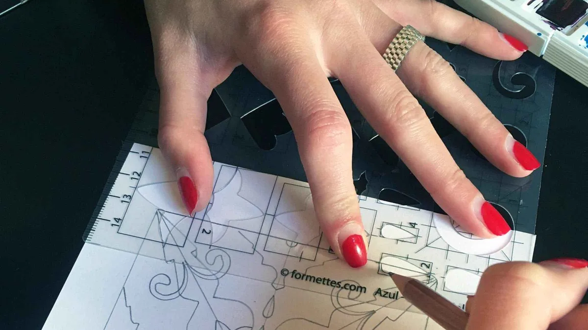 Hands painting a blue geometric pattern on a ceramic tile at an azulejo design workshop in Lisbon