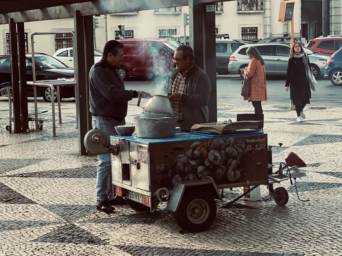 A roast-chestnut cart steaming on a cobbled Lisbon square in the cold months, a dozen chestnuts priced at €2.50 on the trailer